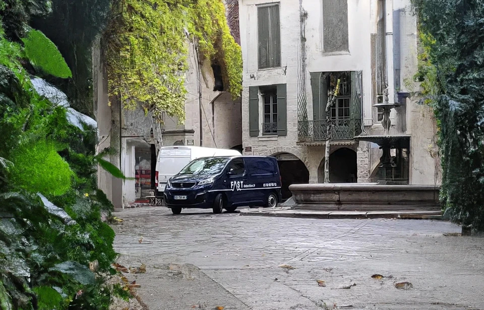 Sc&egrave;ne ext&eacute;rieure urbaine avec agent de s&eacute;curit&eacute; en costume sombre surveillant un v&eacute;hicule berline noire